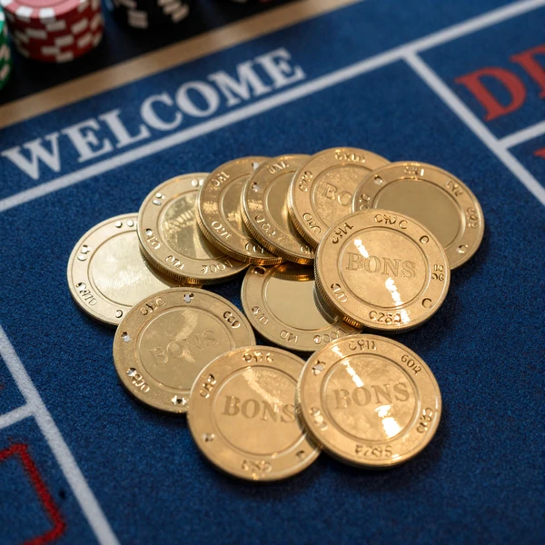 Goldene Willkommensbonus-Casinochips f&auml;cherf&ouml;rmig auf blauem Casinotuch angeordnet